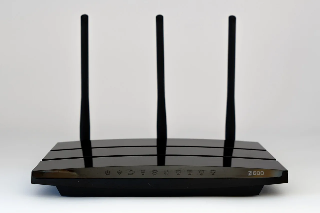 Router de tres antenas visto de frente, con los indicadores luminosos apagados sobre fondo neutro